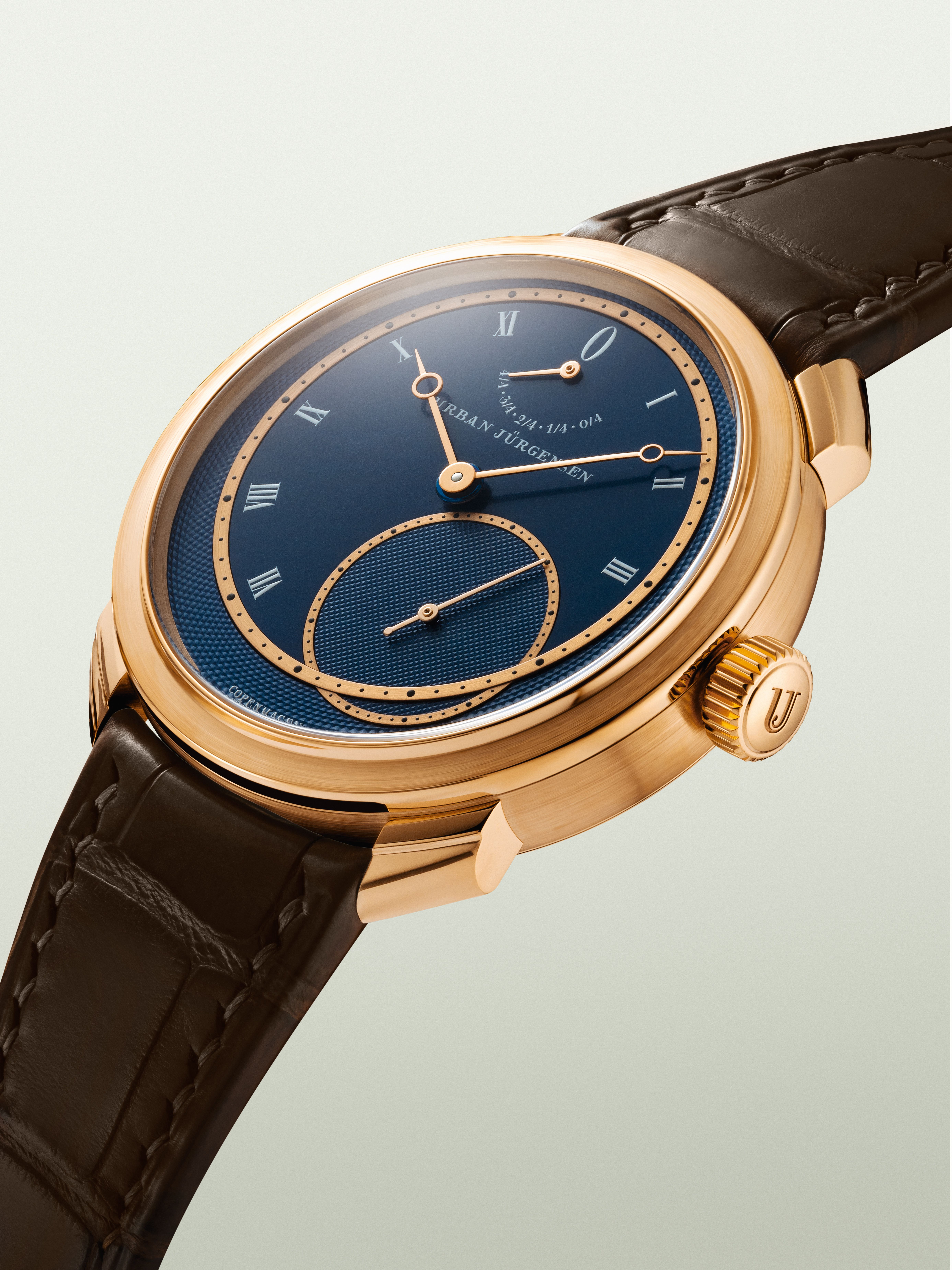 Rose gold Urban Jürgensen wristwatch with deep blue guilloché dial, Roman numerals, power reserve indicator, and brown leather strap.