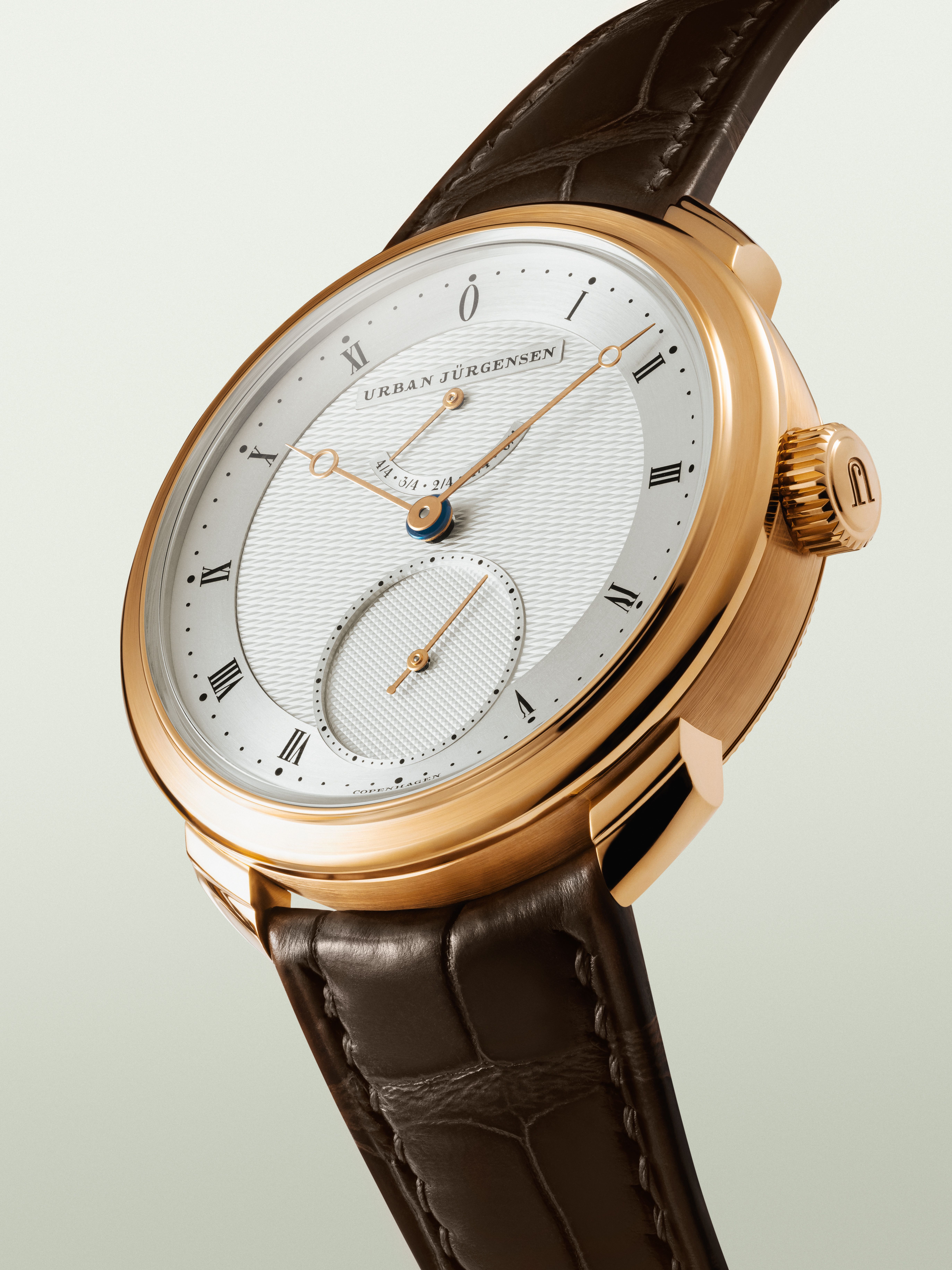 Rose gold Urban Jürgensen watch with guilloché silver dial, gold hands, power reserve, and brown leather strap.