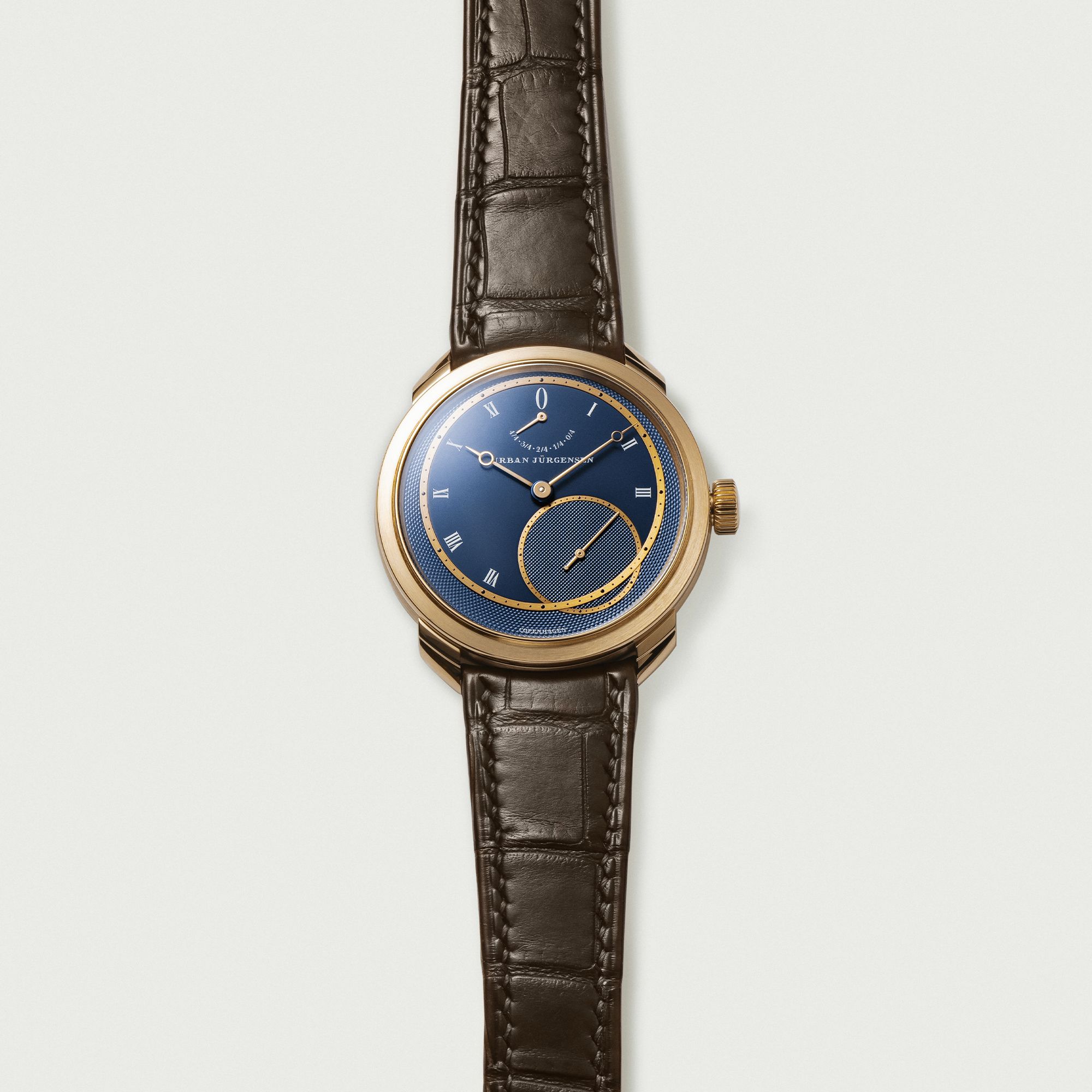 Rose gold Urban Jürgensen wristwatch with deep blue guilloché dial, Roman numerals, power reserve indicator, and brown leather strap.