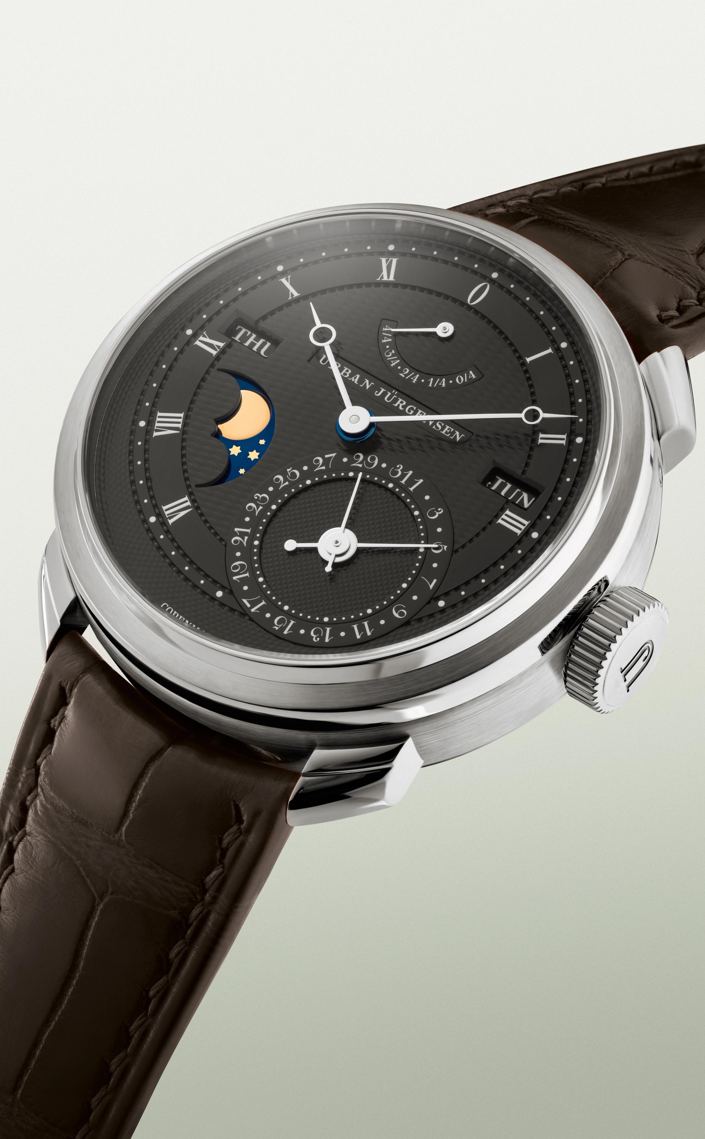 Platinum Urban Jürgensen wristwatch with dark guilloché dial, moonphase, day and date indicators, power reserve display, and brown leather strap.