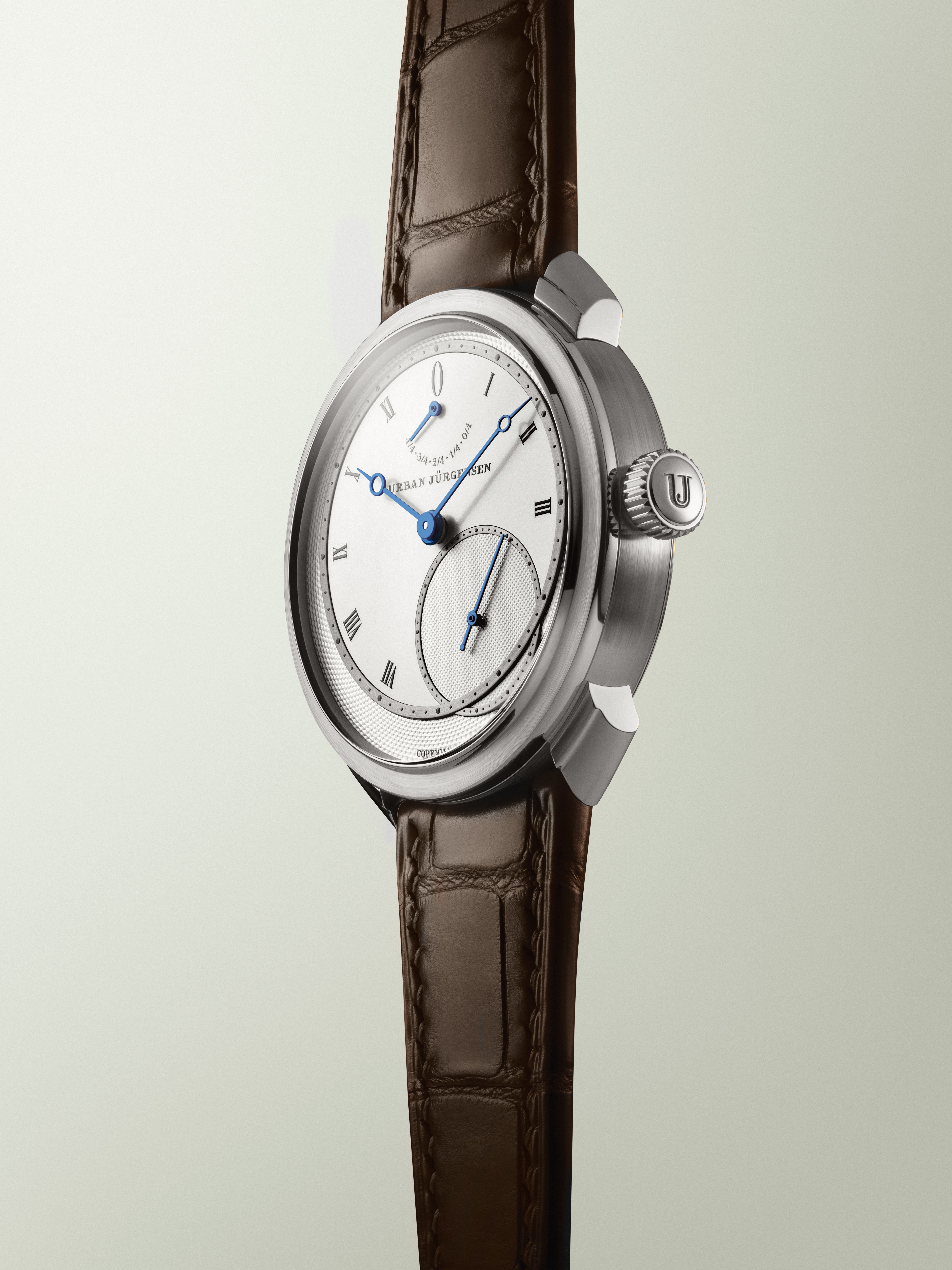 Platinum Urban Jürgensen wristwatch with silver dial, blued hands, Roman numerals, power reserve indicator, and brown leather strap.