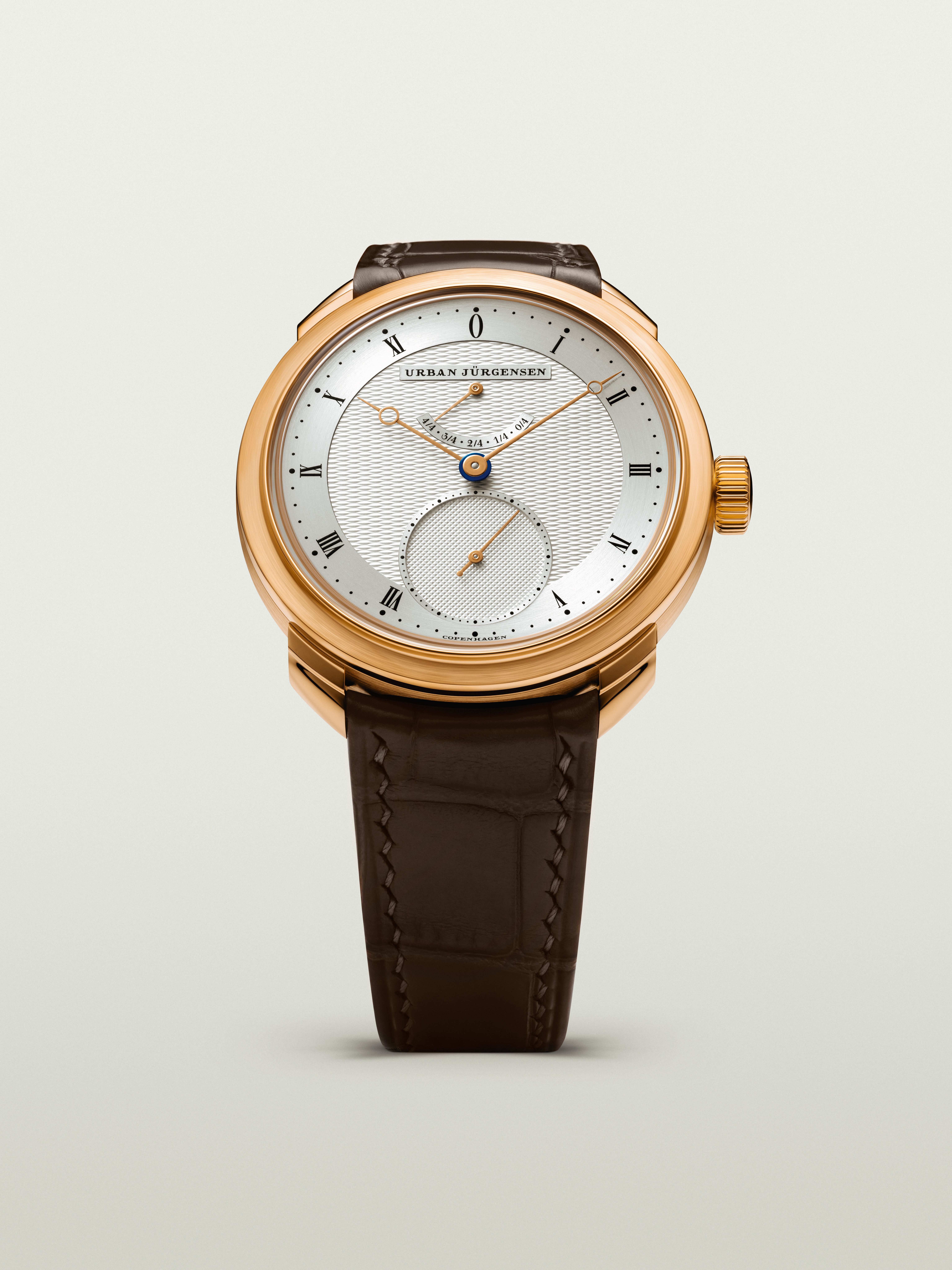 Front view of a rose gold Urban Jürgensen watch with silver guilloché dial, gold hands, power reserve indicator, and brown leather strap.