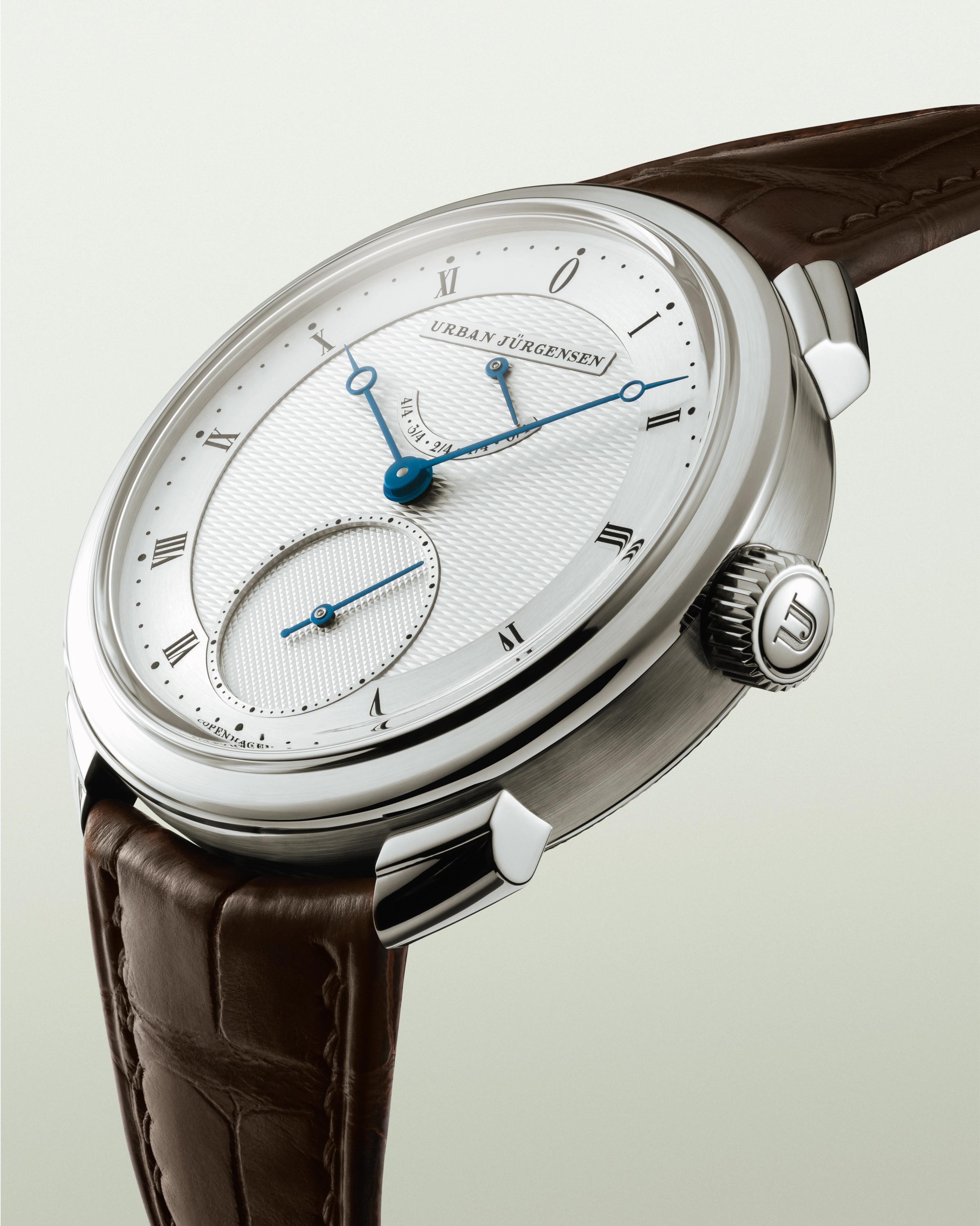 Urban Jürgensen wristwatch with guilloché dial, blue hands, Roman numerals, small seconds subdial, and power reserve indicator.