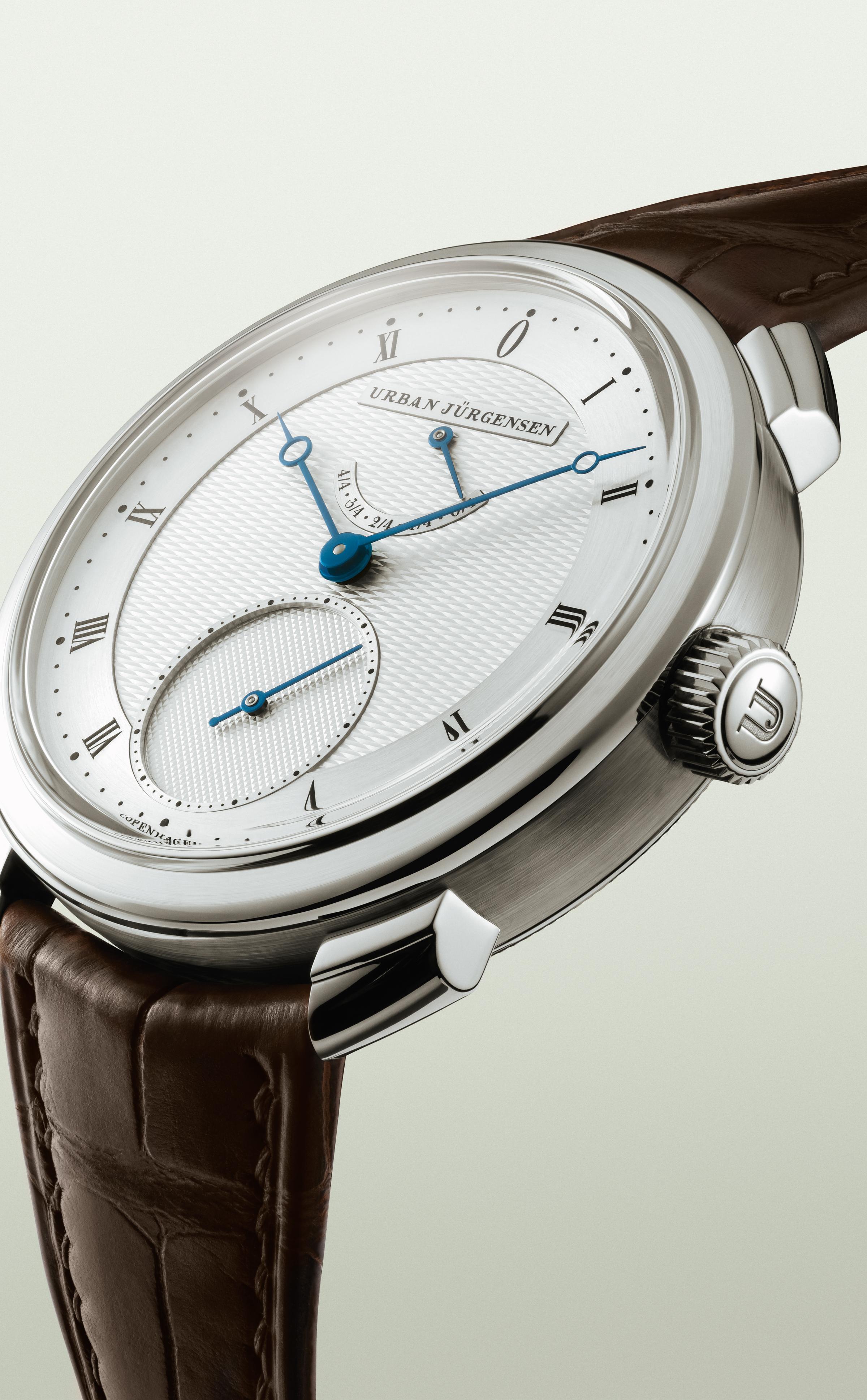 Urban Jürgensen wristwatch with guilloché dial, blue hands, Roman numerals, small seconds subdial, and power reserve indicator.