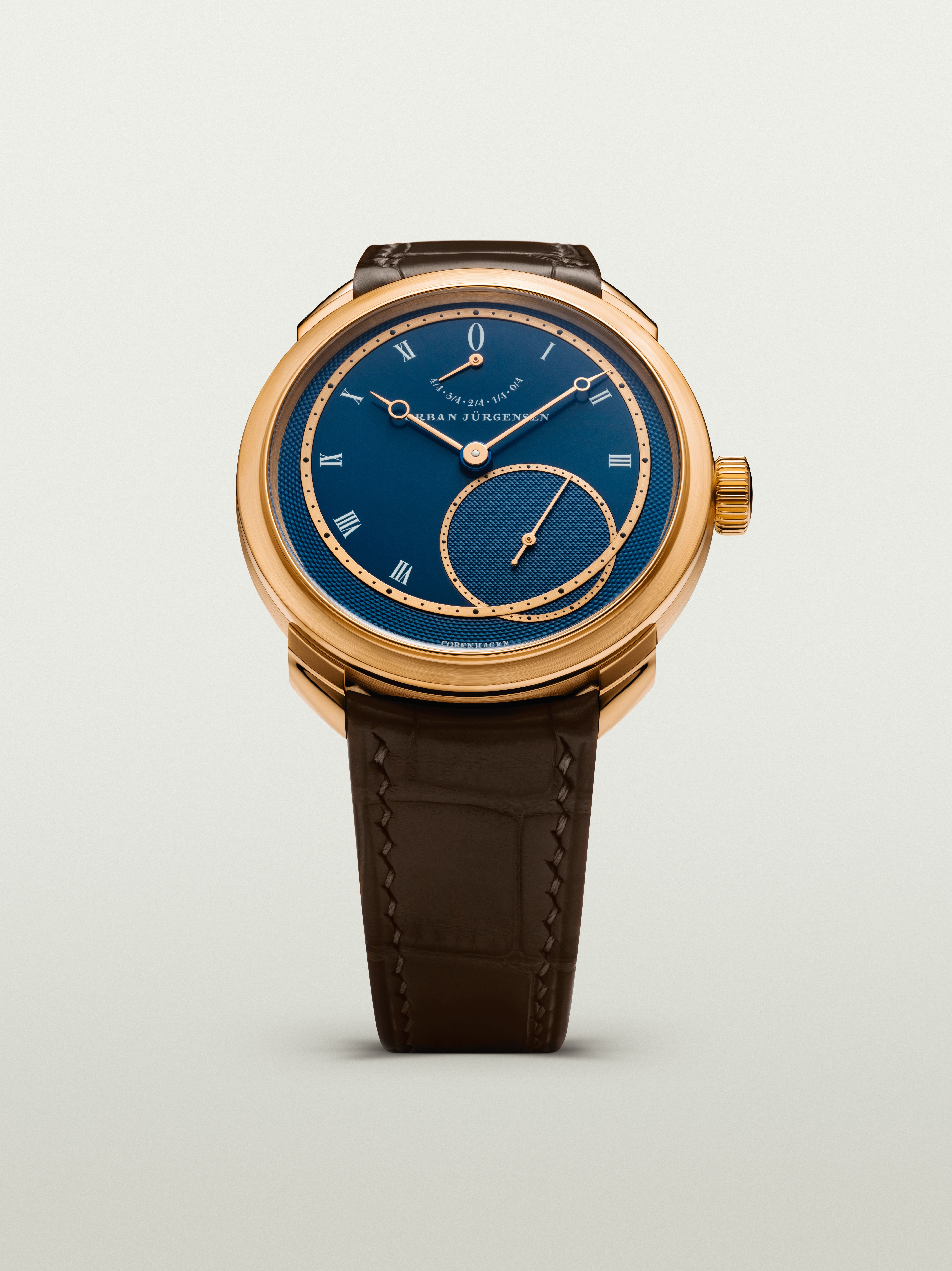 Rose gold Urban Jürgensen wristwatch with deep blue guilloché dial, Roman numerals, power reserve indicator, and brown leather strap.