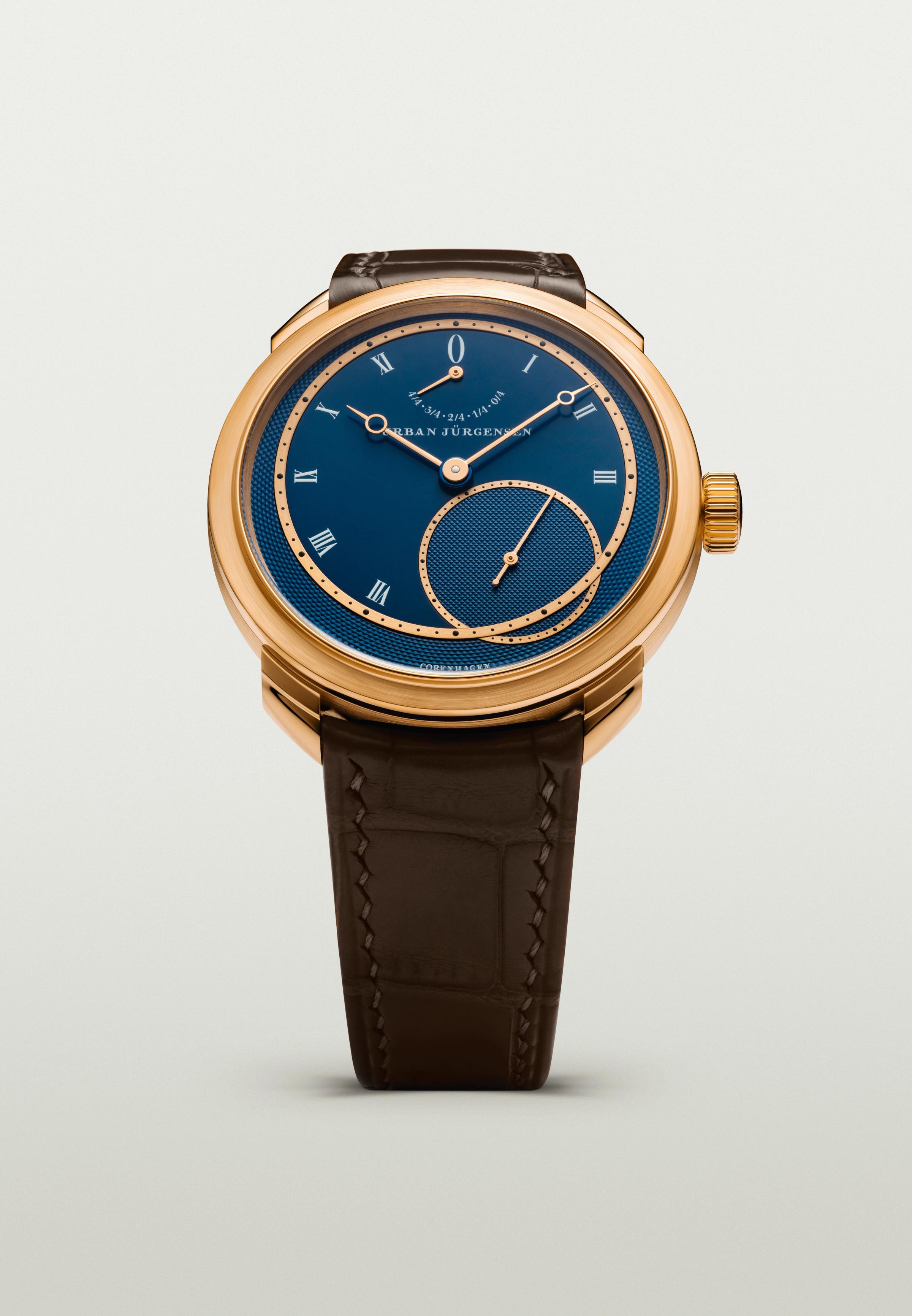 Rose gold Urban Jürgensen wristwatch with deep blue guilloché dial, Roman numerals, power reserve indicator, and brown leather strap.