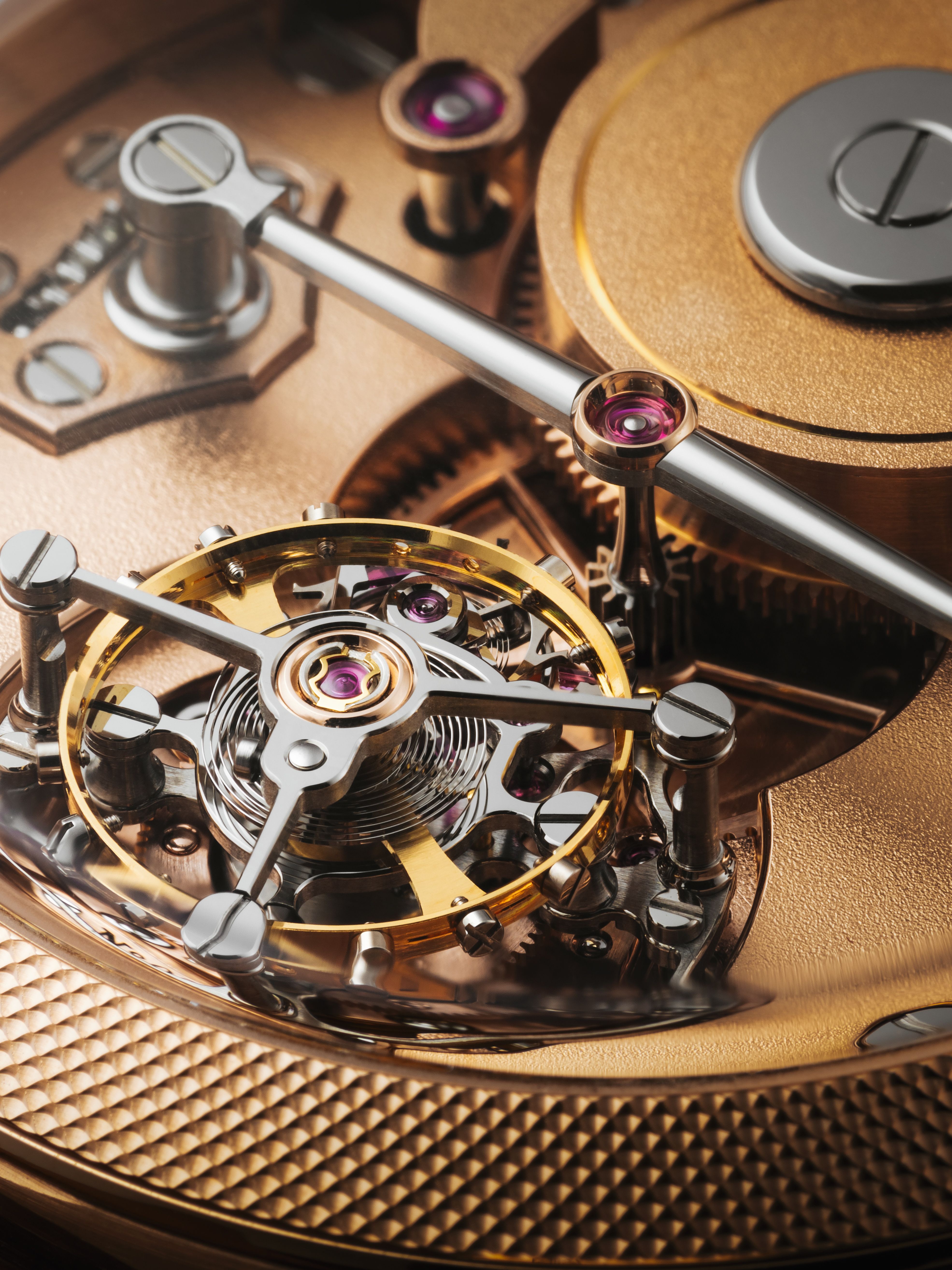 Close-up of a high-end mechanical watch movement showing the balance wheel, bridge, and polished components with gold and steel finishes.