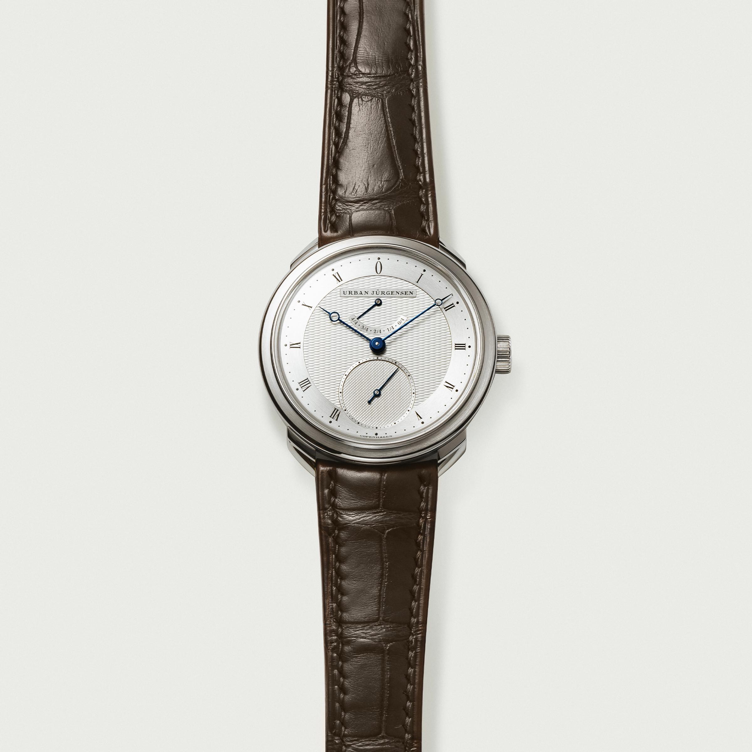 Urban Jürgensen wristwatch with guilloché dial, blue hands, Roman numerals, small seconds subdial, and power reserve indicator.