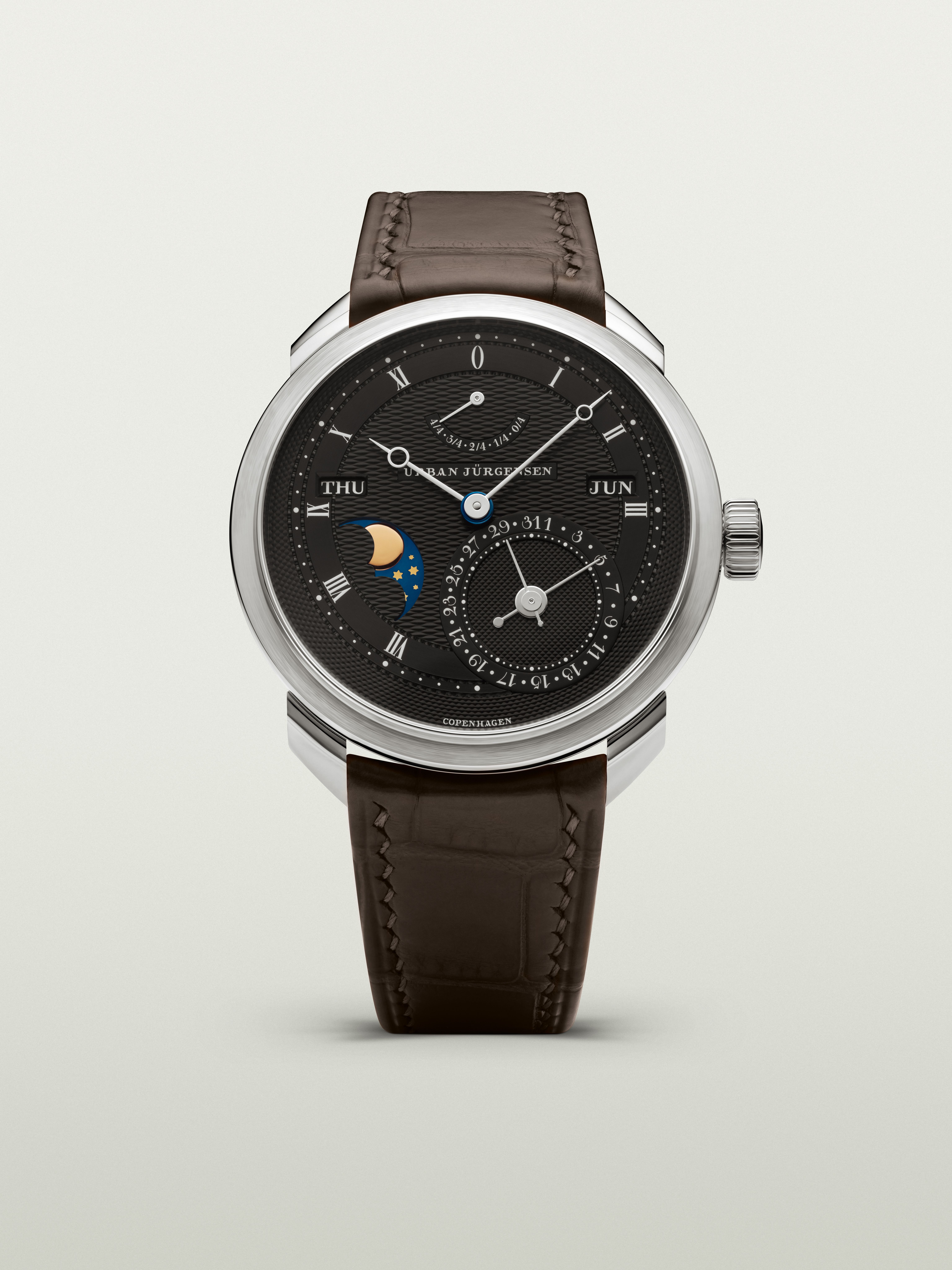Platinum Urban Jürgensen wristwatch with dark guilloché dial, moonphase, day and date indicators, power reserve display, and brown leather strap.