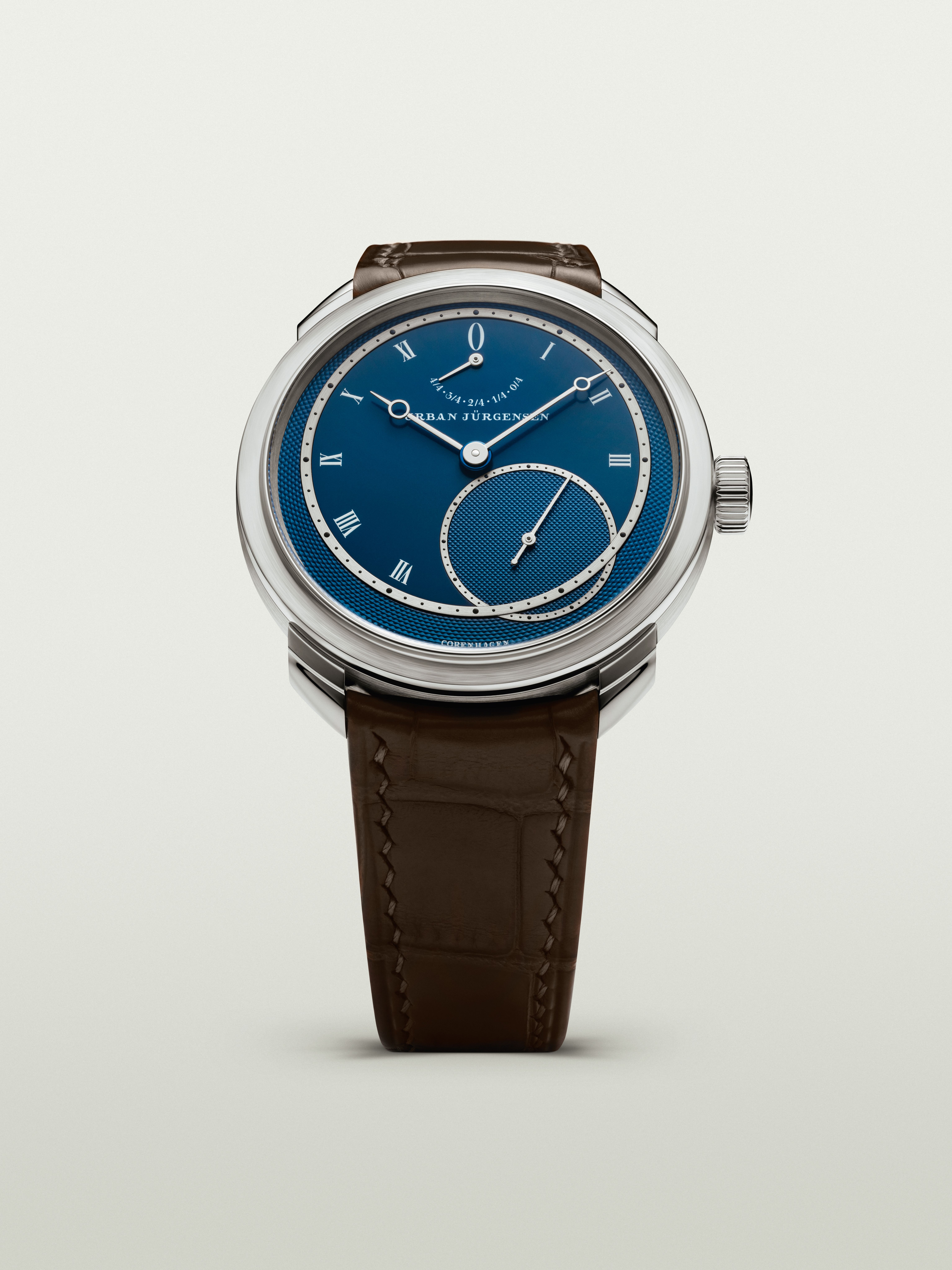 Platinum Urban Jürgensen wristwatch with blue guilloché dial, silver Roman numerals, power reserve indicator, and brown leather strap.