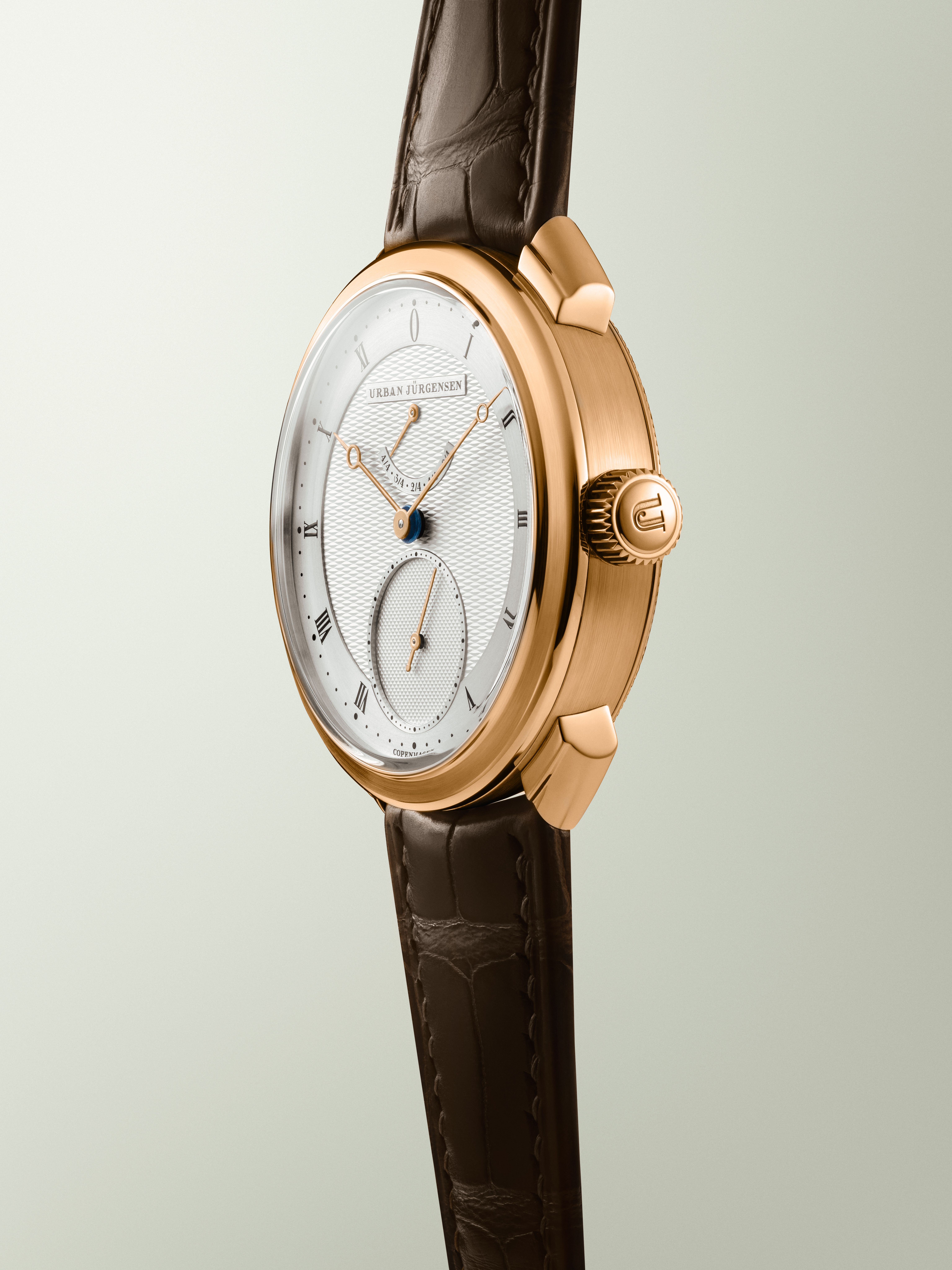 Rose gold Urban Jürgensen watch with guilloché silver dial, gold hands, power reserve, and brown leather strap.