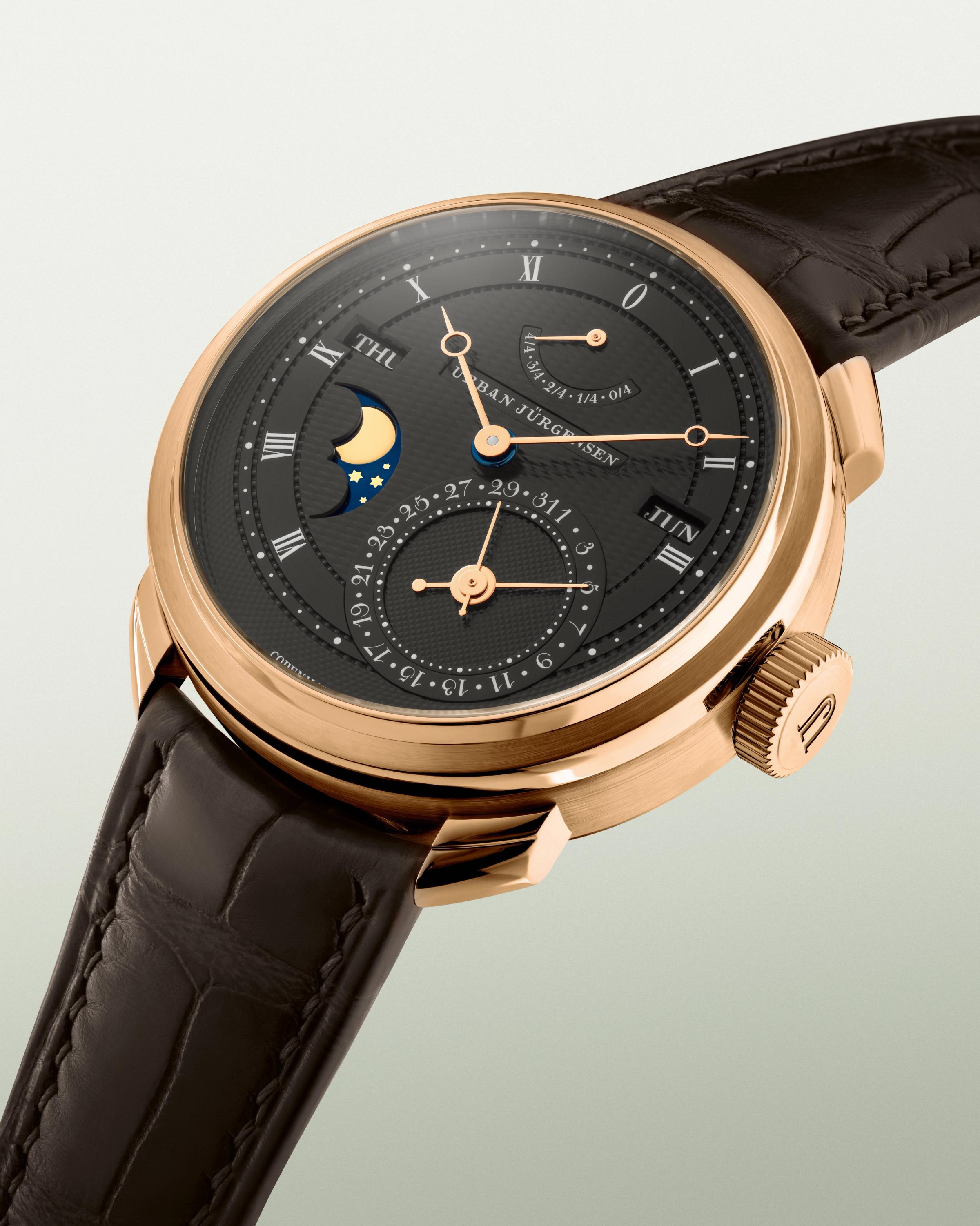 Rose gold Urban Jürgensen wristwatch with dark guilloché dial, moonphase, day and date indicators, power reserve display, and brown leather strap.