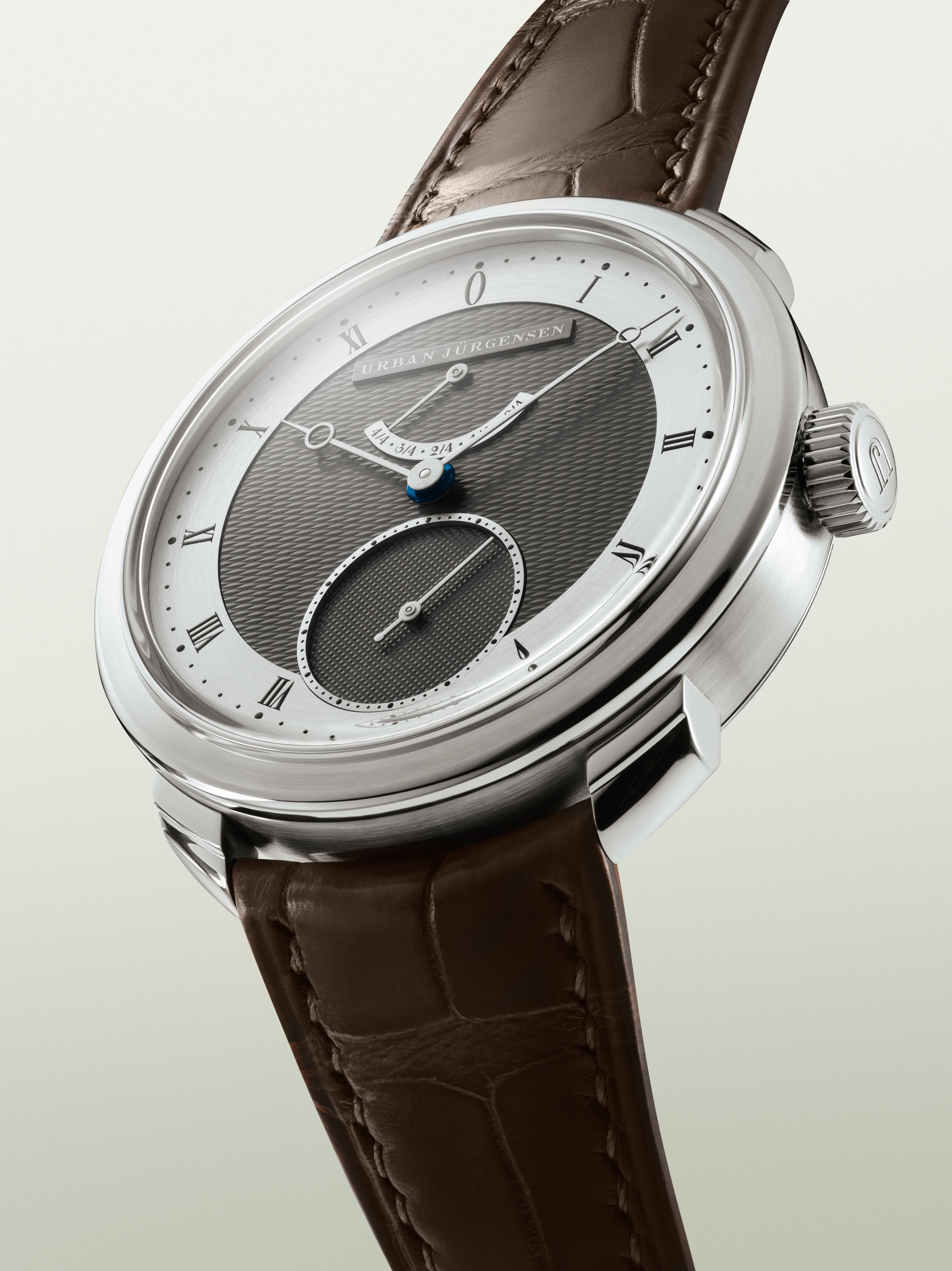 Urban Jürgensen wristwatch with a two-tone guilloché dial, Roman numerals, blued hands, and a brown leather strap.